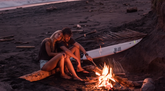 para wtulona w siebie siedzi przy ognisku na plaży