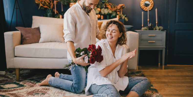 mężczyzna daje kobiecie czerwone róże w domu