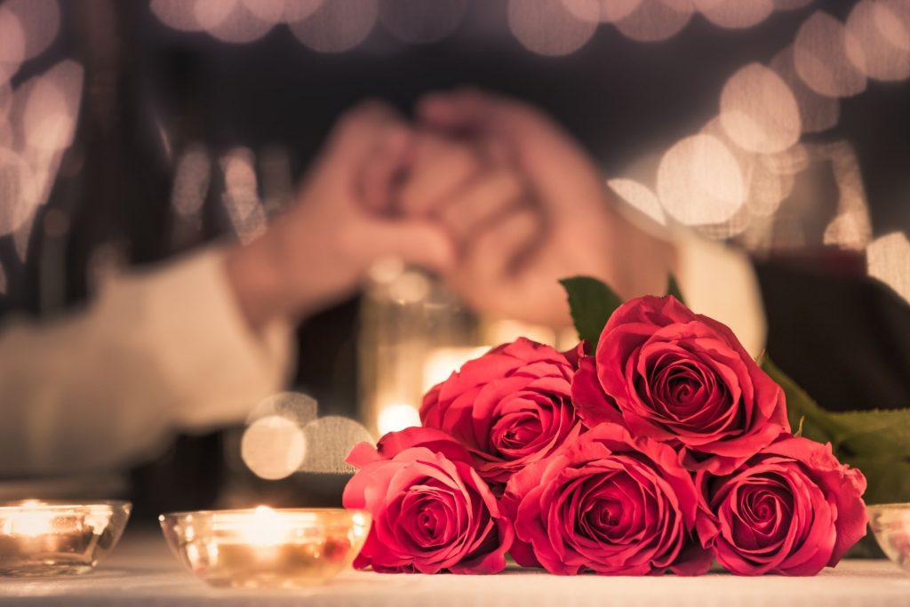 na stole leża róże, a w tle widać parę, która trzyma się za ręce