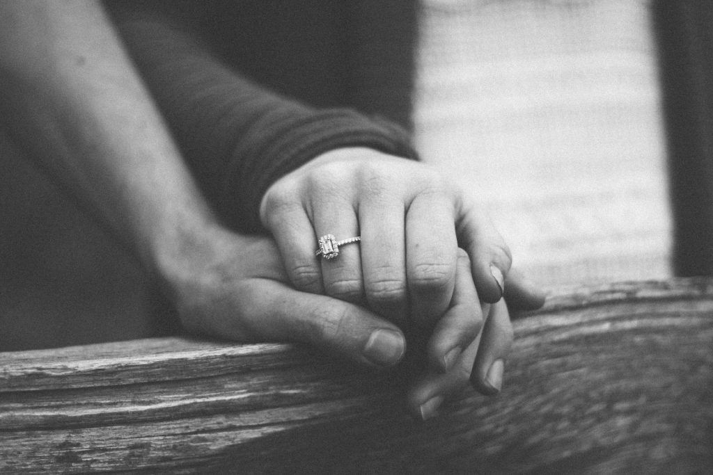 para trzyma się za ręce oparte na drewnianej poręczy, kobieta ma na palcu pierścionek